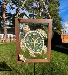 a sea turtle made out of seashells is hanging on a pole in the grass