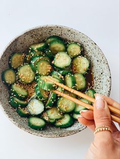 a woman is holding chopsticks over a bowl of cucumbers and sesame seeds