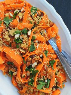 a white plate topped with carrots and nuts next to a silver fork on top of a wooden table