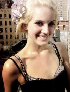 a woman with blonde hair wearing a black dress and flower in her hair smiling at the camera