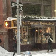 the corner bookstore is covered in snow as people walk down the street with umbrellas