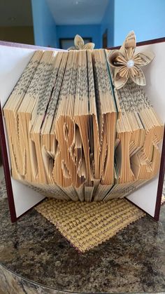 an open book folded into the shape of a house with flowers on it, sitting on top of a table