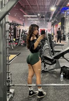 a woman taking a selfie in the gym with her cell phone while wearing high waisted shorts