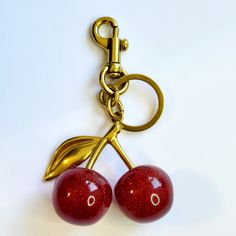 two red cherries attached to a gold colored keychain on a white surface