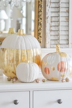 two white pumpkins sitting on top of a dresser next to a gold painted mirror