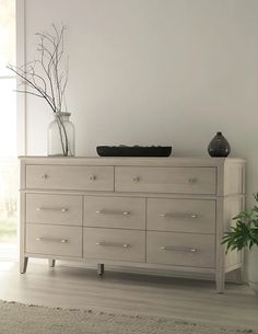 a white dresser sitting in front of a window next to a potted plant on top of a table