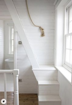 a white staircase leading to a bathroom with a rope hanging on the wall next to it