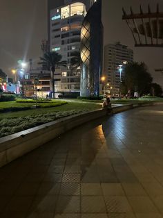 a man riding a motorcycle down a street next to tall buildings in the background at night