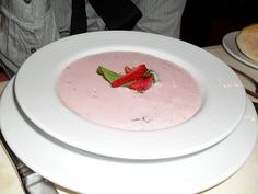 a white plate topped with a pink soup and garnished with a green leaf