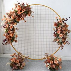 an arrangement of flowers arranged in front of a round metal frame on the floor next to a wall