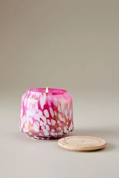 a pink and white candle sitting on top of a table next to a wooden coaster