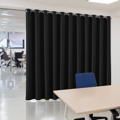 an empty conference room with black curtains and blue chairs in front of the desks