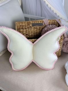 a white and pink butterfly pillow sitting on top of a bed next to a basket