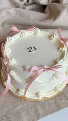 a white cake with pink ribbon and number 25 on the top is sitting on a table