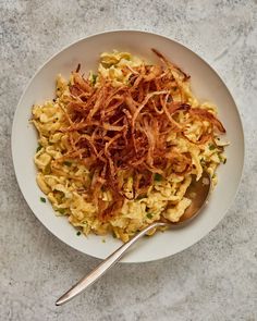 a white plate topped with macaroni and cheese covered in shredded meat next to a spoon