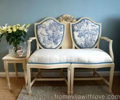 a white couch sitting next to a vase with flowers on top of it in front of a blue wall