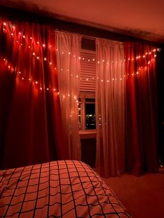 a bedroom with red curtains and lights on the window sill, bed in foreground