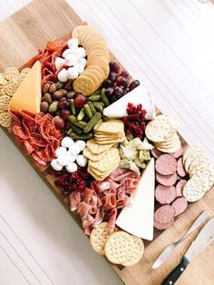 a wooden cutting board topped with cheese, crackers and meats