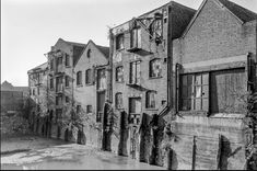 black and white photograph of an old brick building with water running down the street in front of it