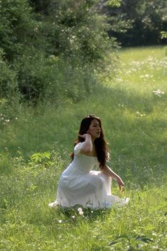 a woman in a white dress sitting on the grass with her hands behind her head