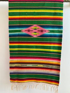 a multicolored blanket hanging on a clothes line with a white wall in the background