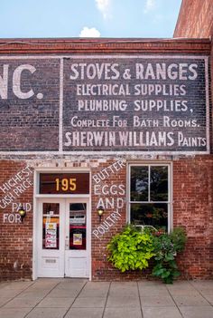 an old brick building with signs on the front door and windows that read, stoves & ranges electrical supplies plumbing supplies, complete for bath rooms shewn williams paints