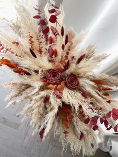 an arrangement of dried flowers and leaves on a white background with red roses in the center