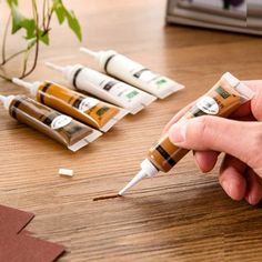 a person is holding three tubes of glue on a wooden table next to some plants