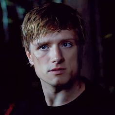 a man with blonde hair and blue eyes staring at the camera while wearing a black t - shirt