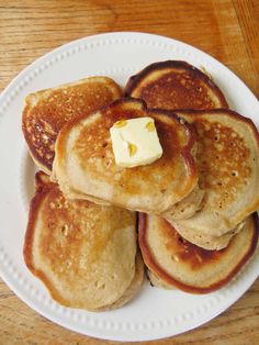 pancakes with butter and syrup on a white plate sitting on a wooden table, ready to be eaten