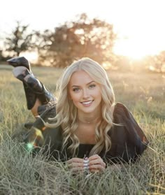 a beautiful blond woman laying in the grass with her feet up and smiling at the camera