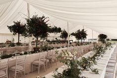 tables and chairs are set up in a tent with white linens, flowers and greenery