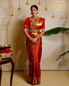 a woman in a red and gold saree standing next to a table with flowers on it