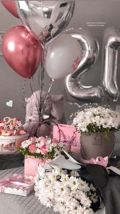 a table topped with lots of pink and white flowers next to balloons in the shape of numbers