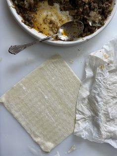 a white bowl filled with food next to a piece of parchment paper and a spoon