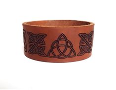 Trinity Knot Leather Cuff Bracelet This full grain cowhide leather bracelet is laser engraved with Trinity knot design. The Trinity knot design first appears in the historical record around 400AD when Coptic missionaries traveled to Ireland and proceeded to produce the highly esteemed Illuminated manuscripts. It symbolizes the three fold Godhead - the three points represents Father, Son and Holy Ghost and the interwoven circle depicts the unity between the three. *To measure the right size for y Engraved Brown Leather Bracelet, Brown Engraved Leather Bracelet, Brown Engraved Leather Cuff Bracelet, Brown Leather Engraved Cuff Bracelet, Engraved Leather Bracelets, Three Fold, Leather Cuff Bracelet, Trinity Knot, The Trinity