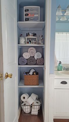 a bathroom with blue walls and shelves filled with toilet paper, towels and other items