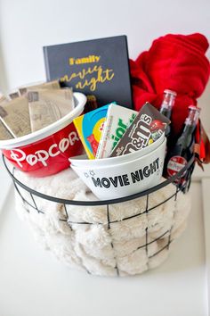 a basket filled with movies and snacks on top of a white table next to a red rose