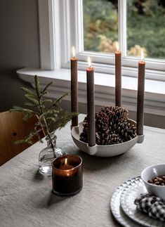 the candles are lit on the table with pine cones and other decorations in front of it