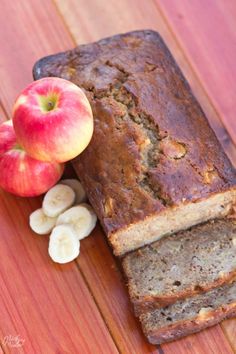 a loaf of banana bread next to sliced bananas and an apple on a wooden table