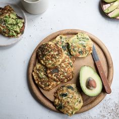 an avocado and some pancakes on a wooden plate with a knife next to it