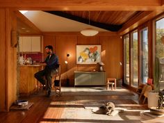 a man sitting on a chair in a room with wood paneling and large windows