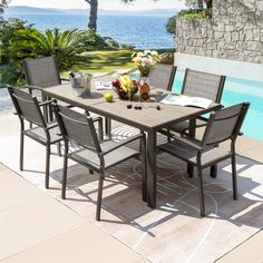 an outdoor dining table with six chairs next to a swimming pool and ocean in the background