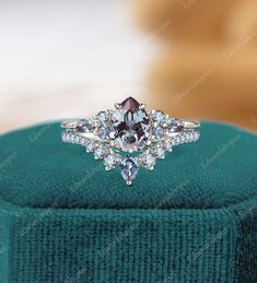 an engagement ring with purple and white diamonds on top of a green velvet cushioned box