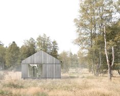 a small wooden house in the middle of a field with trees and grass around it