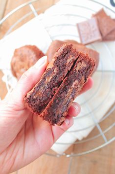 a hand holding a piece of chocolate brownie in front of a plate with two pieces on it