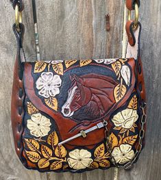 a brown leather purse with a horse and flowers on the front is hanging on a wooden wall