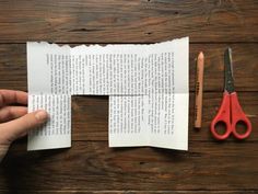 someone is cutting out an open book with scissors and pencils next to it on a wooden table