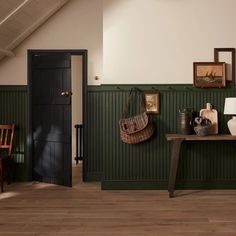 a room with green walls and wooden flooring in the center is a table, two chairs, vases on either side