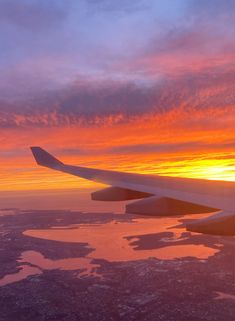 the wing of an airplane as it flies over water and land at sunset or dawn